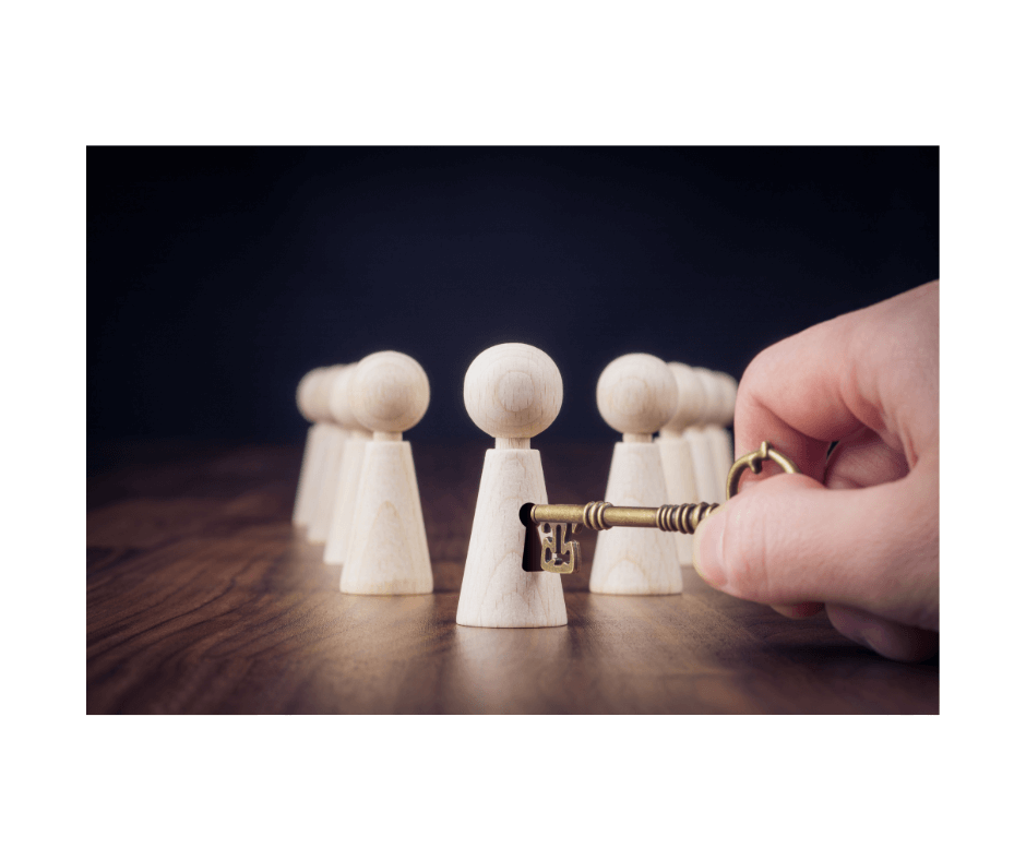 A hand holding a golden key in front of wooden figurines on a table, symbolizing access.
