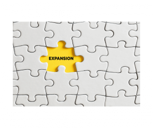 A white puzzle with one yellow missing piece labeled "EXPANSION," symbolizing Amazon global marketplaces.